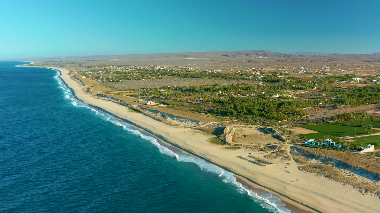 Aerial beach scene with blue ocean, breaking waves, dunes, and inland vegetation