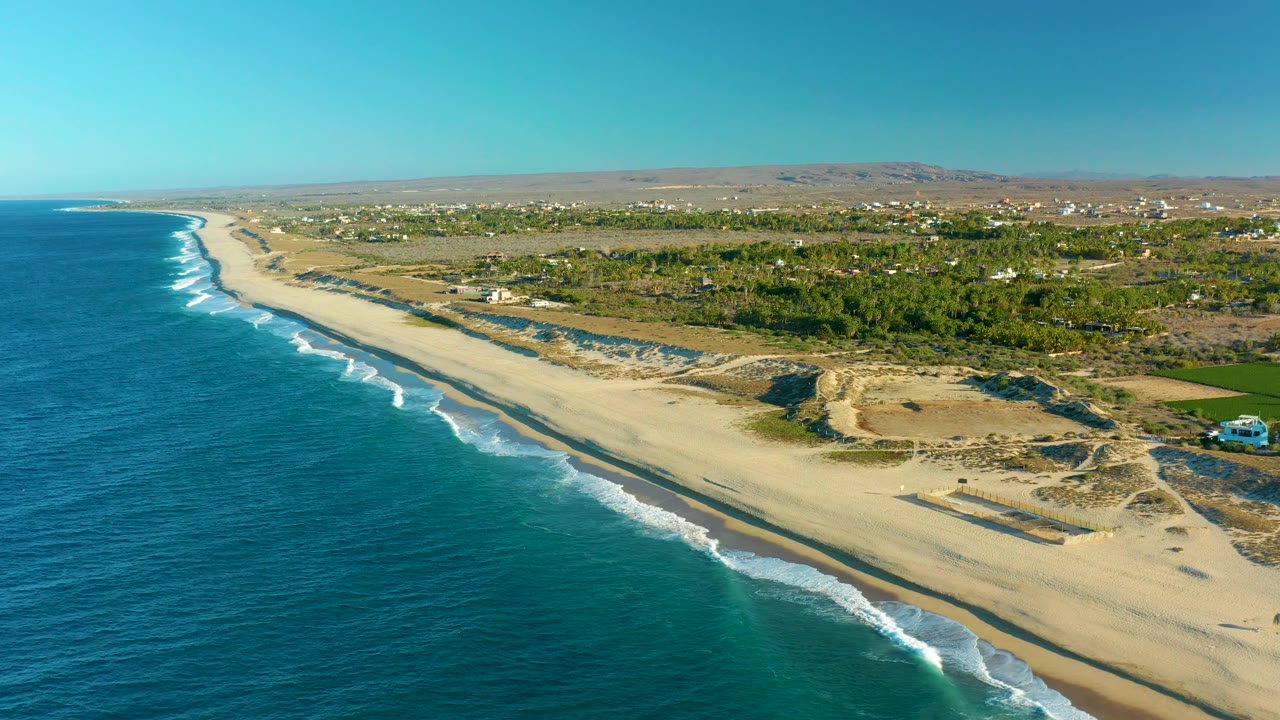 Ocean surf breaking along a sandy beach with greenery inland.