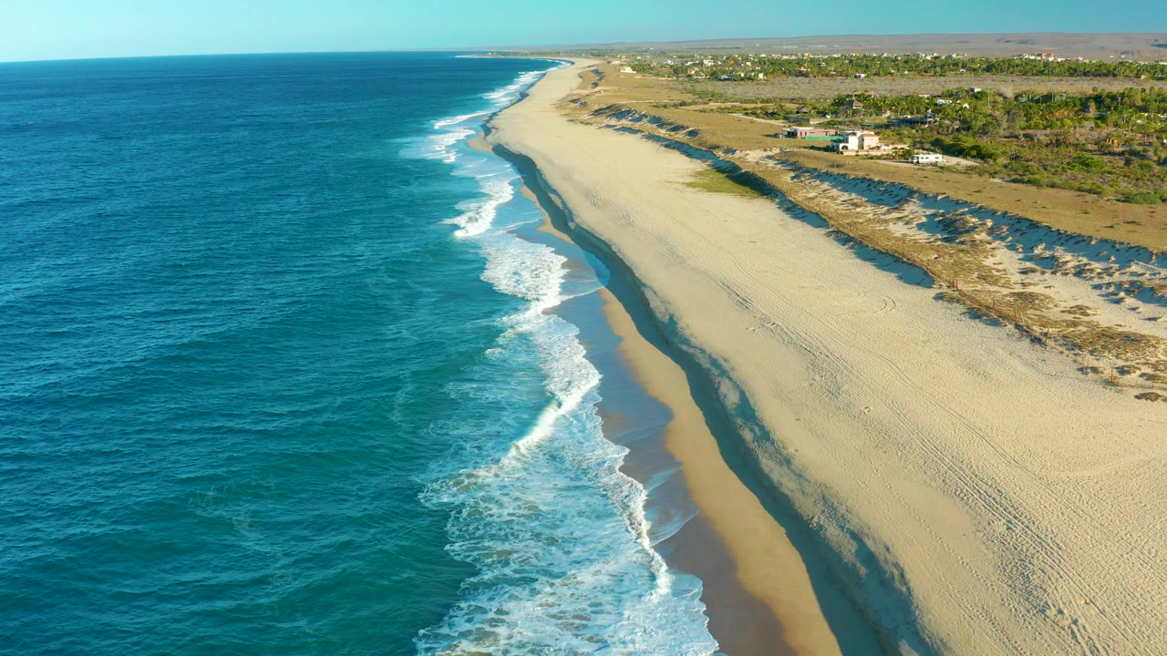 Aerial coastline with ocean on one side and broad empty beach on the other.