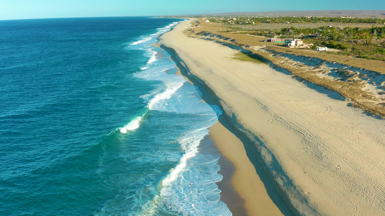 Blue ocean and white surf beside a long sandy shoreline.