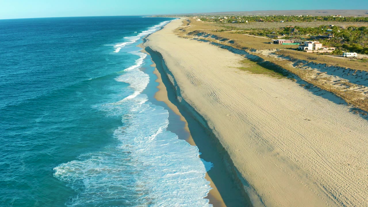 Breaking waves wash diagonally along an empty beach.