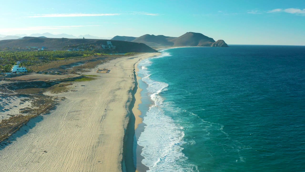 Aerial view of a sandy beach with ocean waves and inland vegetation.