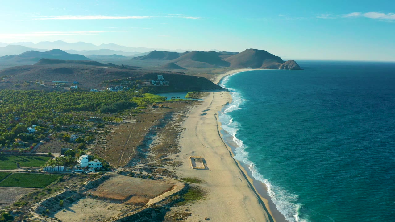 The second frame holds the Todos Santos shoreline from above, with white wave bands along the sand, inland greenery to the left, hazy mountain layers beyond, and no visible people.