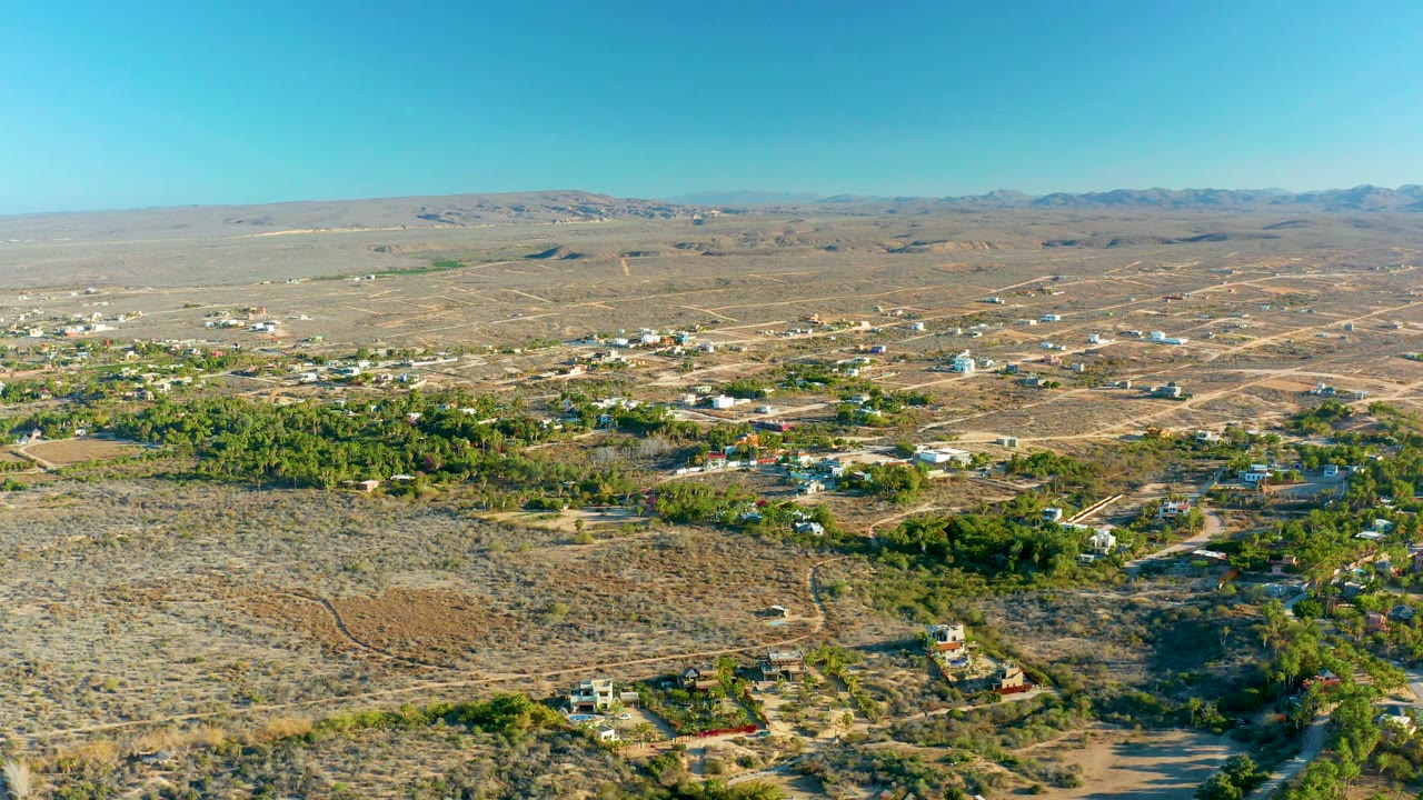 Aerial panorama of dry settlement roads with green trees and hills beyond.