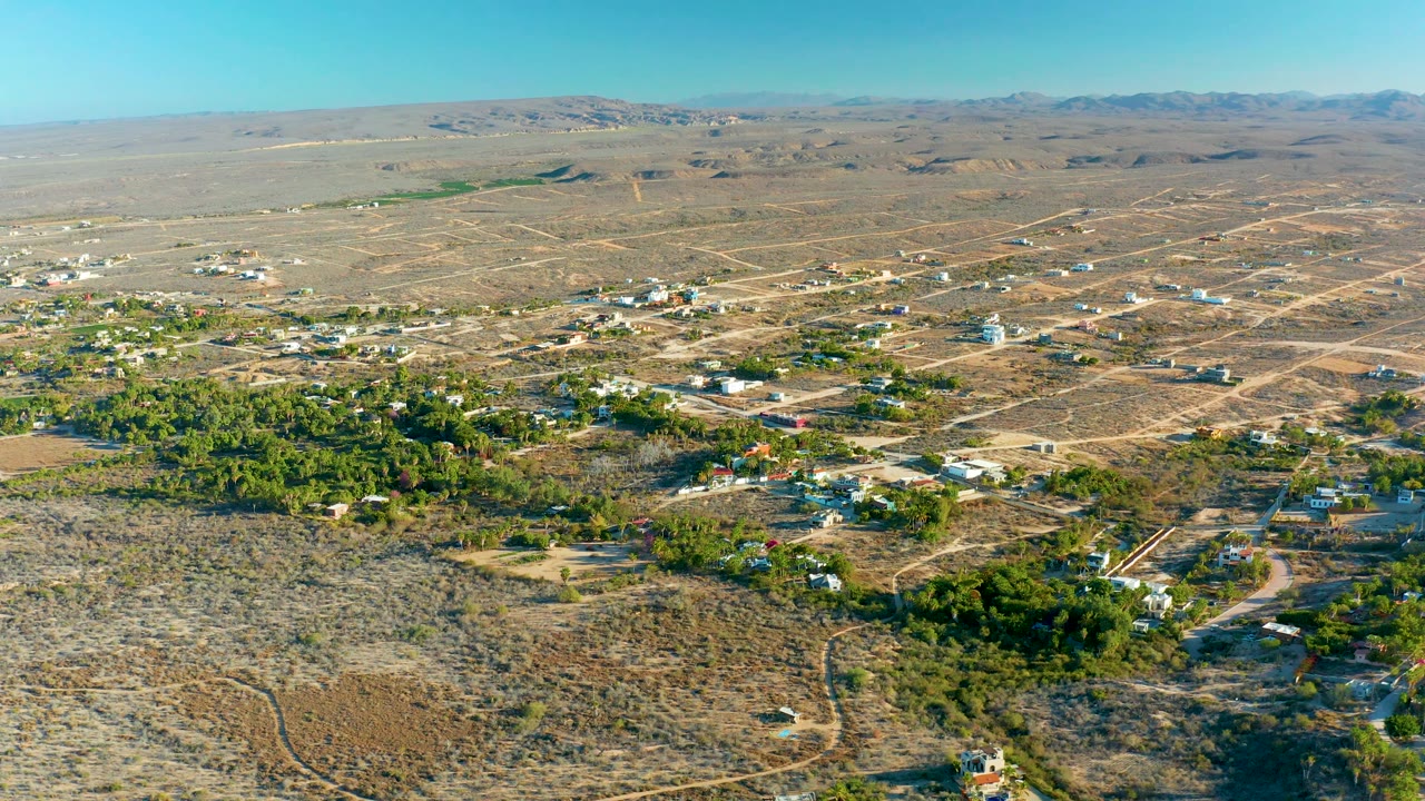 Aerial desert community with scattered houses, road tracks, trees, and hills.