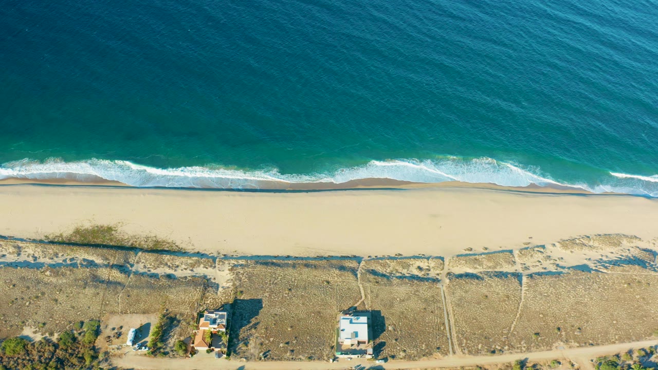 Overhead wave breaking along a sandy shore with dry land and homes below.