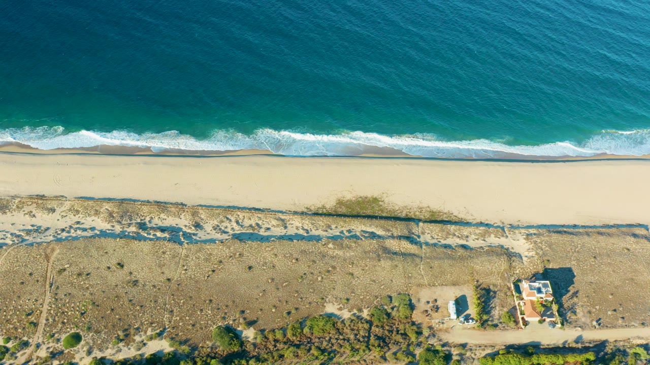 Overhead sandy beach with turquoise waves and dry dunes below the shore.