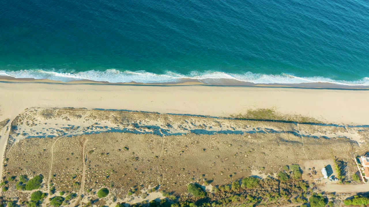 Overhead beach with turquoise water, surf, sand, and dunes.