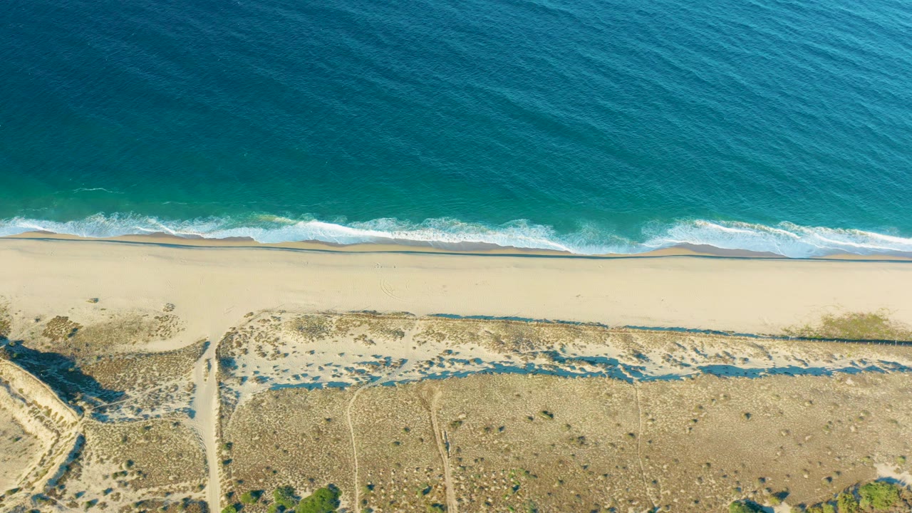 Overhead beach, turquoise ocean, sand, dunes, and paths.