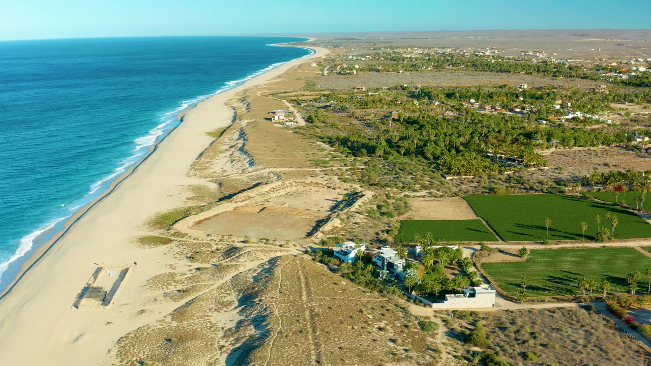 Coastal fields and dunes beside a long sandy beach and blue ocean.