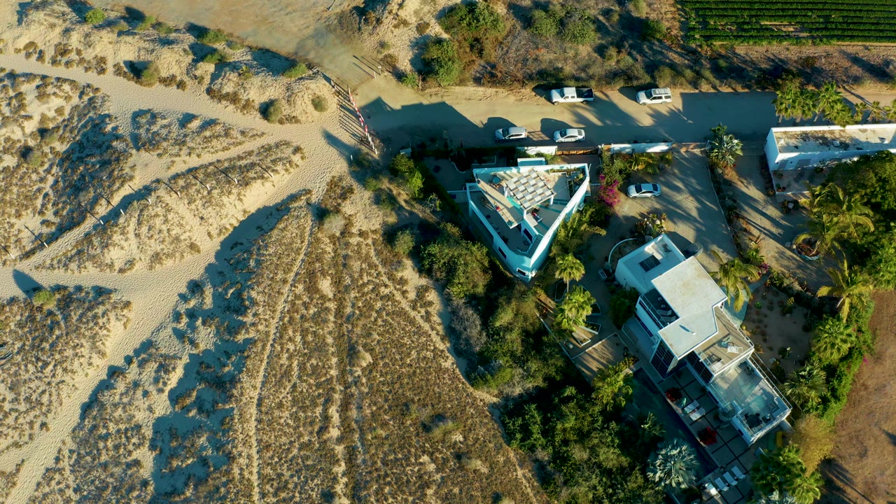 Aerial view of dunes, a road, parked vehicles, and homes near vegetation.