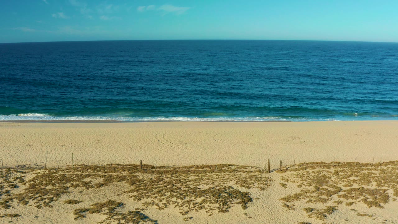Wide aerial view of blue ocean, pale beach, and low dunes