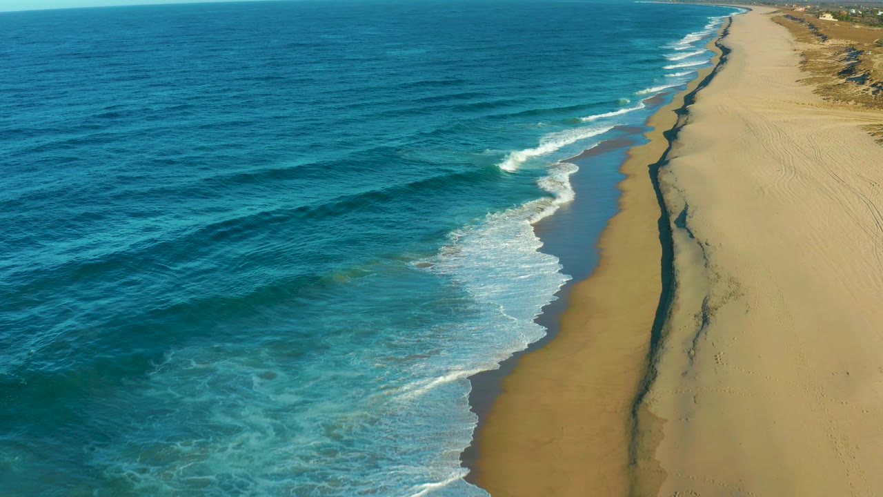 Aerial coastline with surf bands running along wet sand.