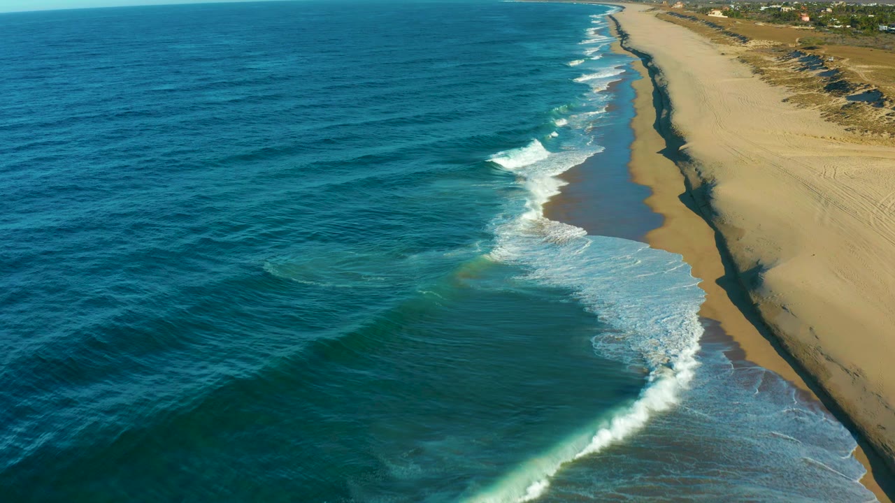 Foamy surf spreads across wet sand beside open ocean.