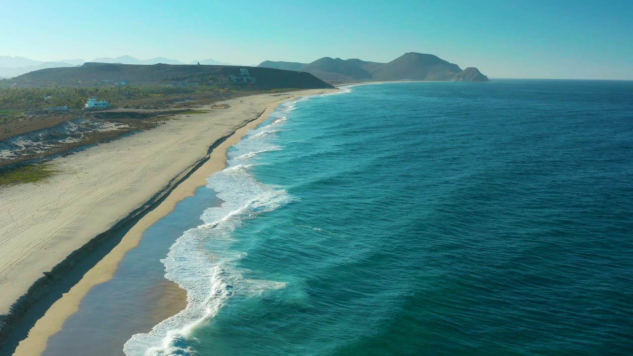 Drone view of a sandy beach with waves meeting the shore.
