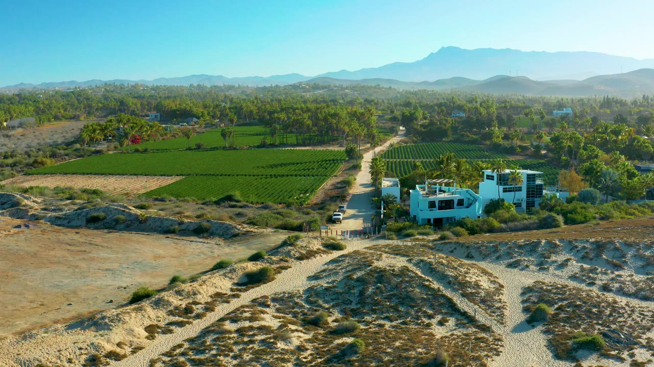 Aerial farmland scene with dry foreground, dirt road, and white building.