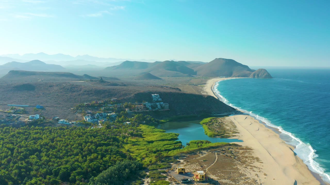 High coastal aerial with lagoon and forest in foreground and waves along beach.