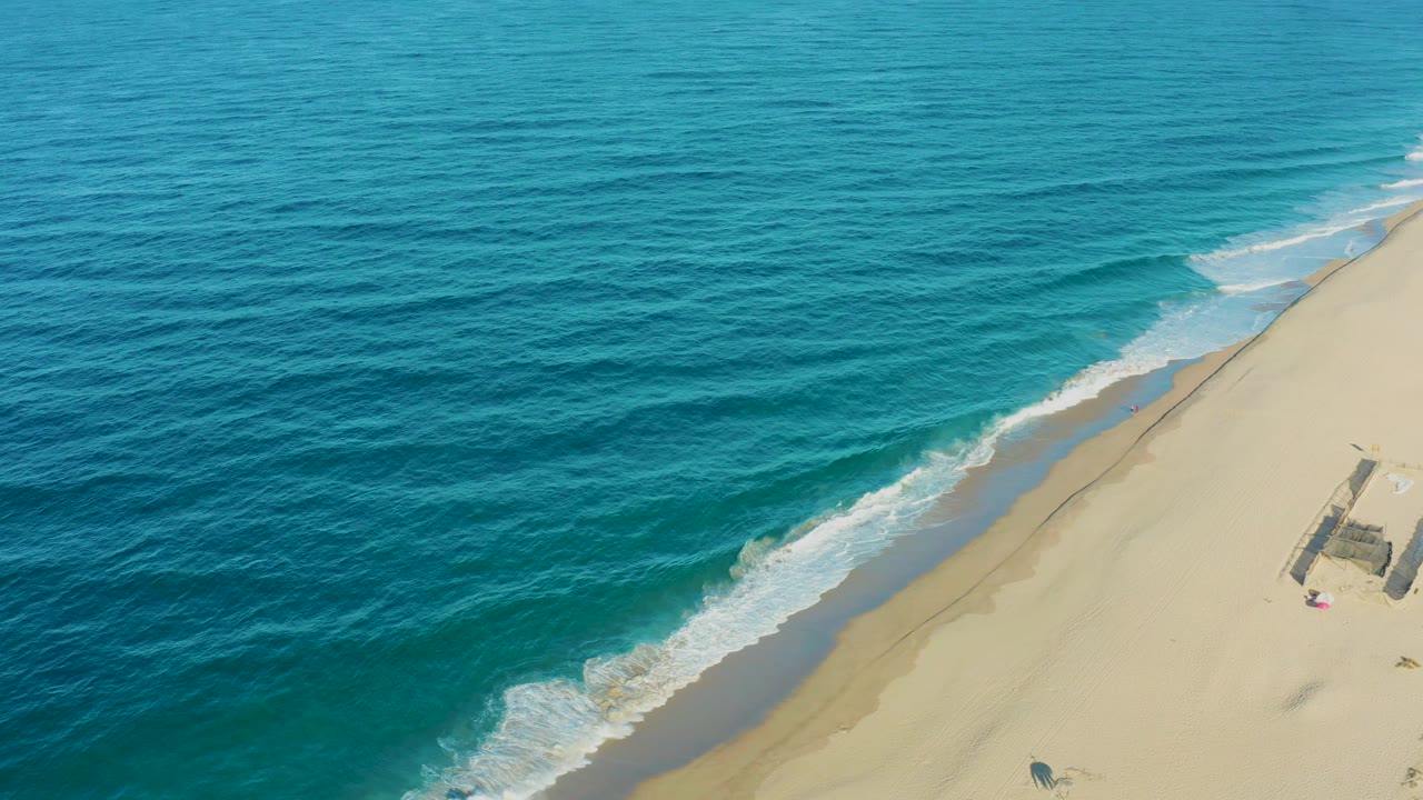 The Todos Santos shoreline remains angled through the frame as a thin band of white foam slides along the sand, with no visible people.