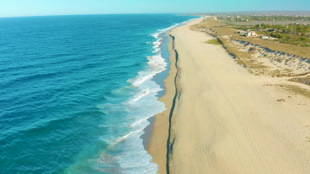 High aerial beach view with ocean waves and dune-backed sand.