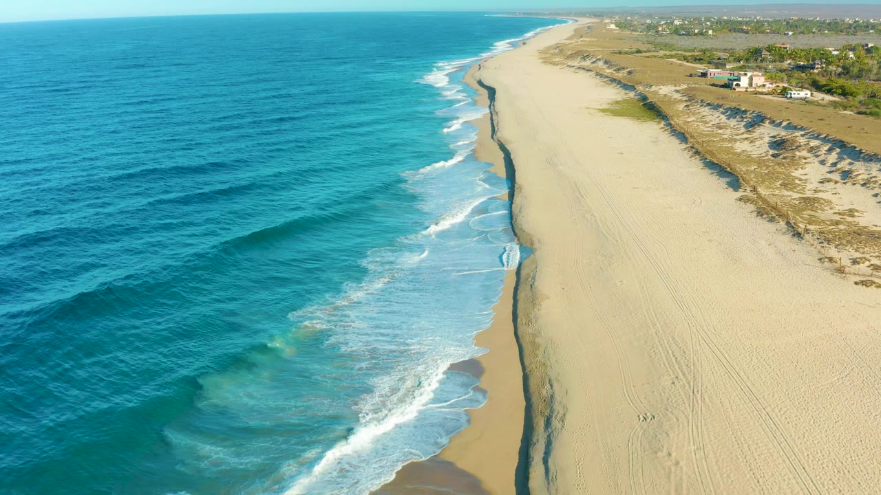 Aerial coastline with waves washing onto an empty sandy beach.