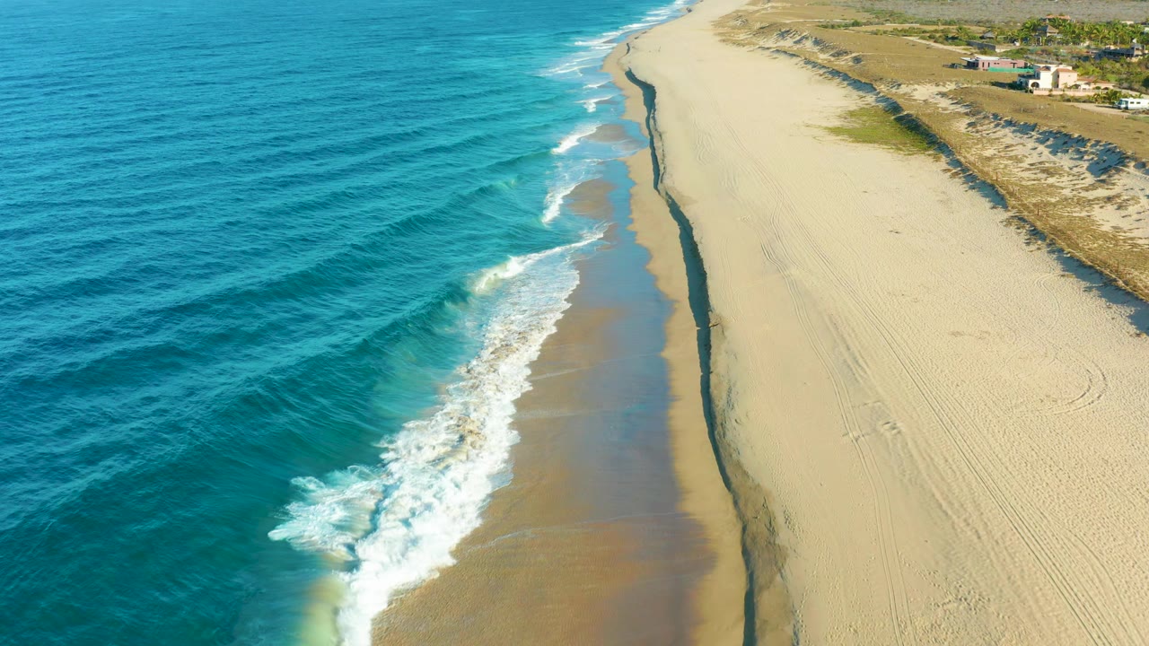 Oblique aerial view of waves rolling onto an empty sandy beach.