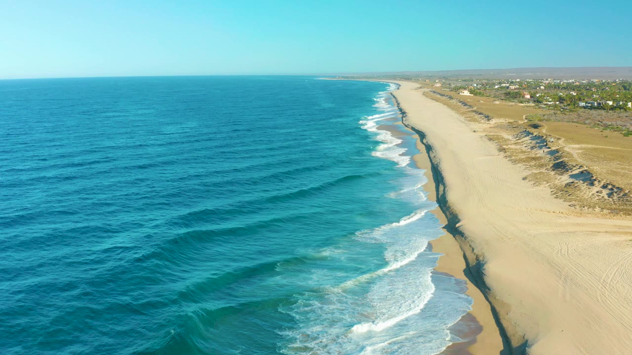 Aerial coastline with ocean waves rolling onto empty sand.