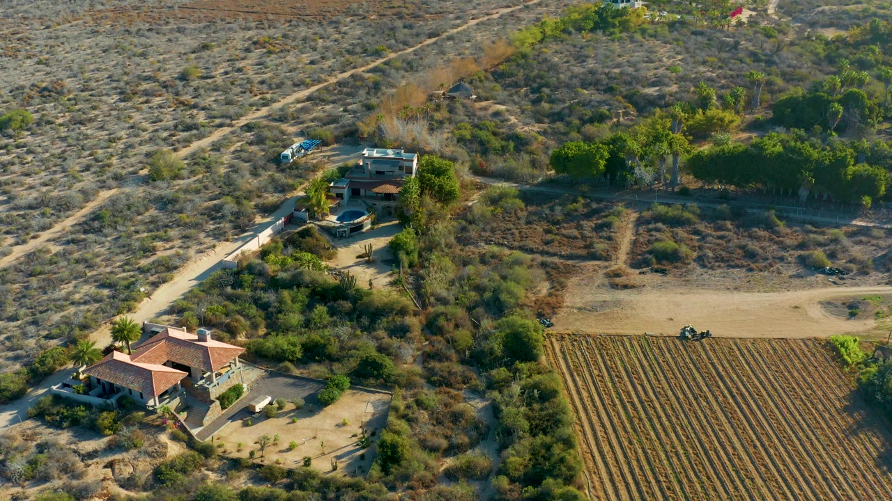 Aerial view of a red-roofed house near a dirt road and plowed field.