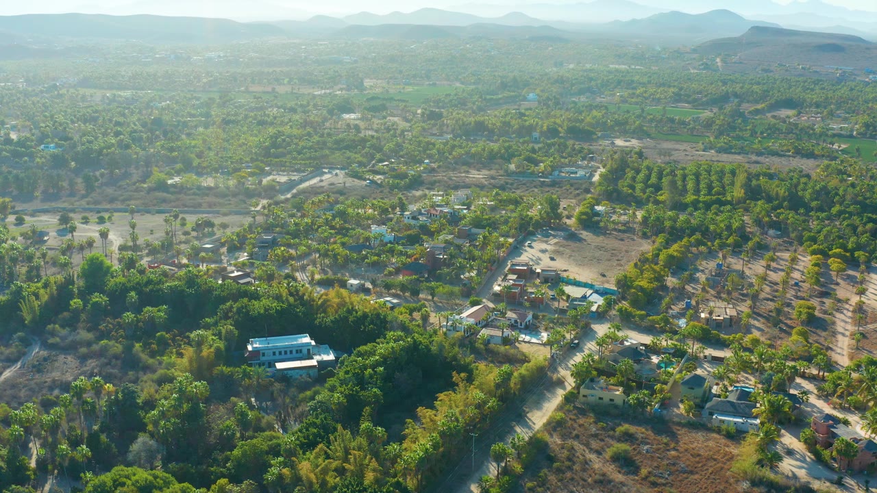 Aerial landscape with a white-roofed building, homes, fields, and tree cover.