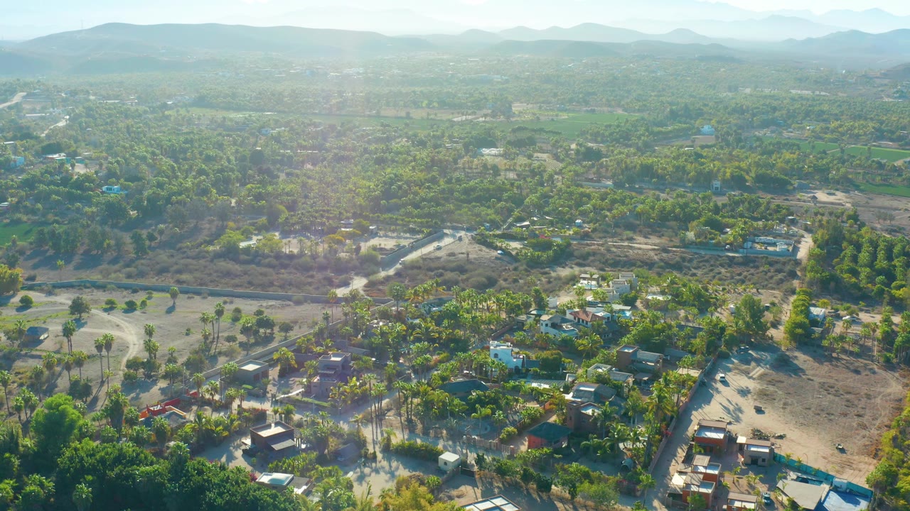 Aerial landscape of homes, trees, roads, open land, and mountains.