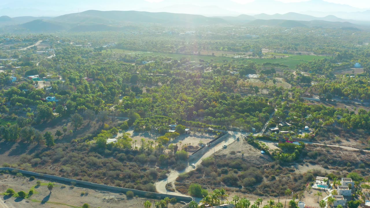 Aerial landscape with winding road, scrub, palms, houses, and distant ridge.