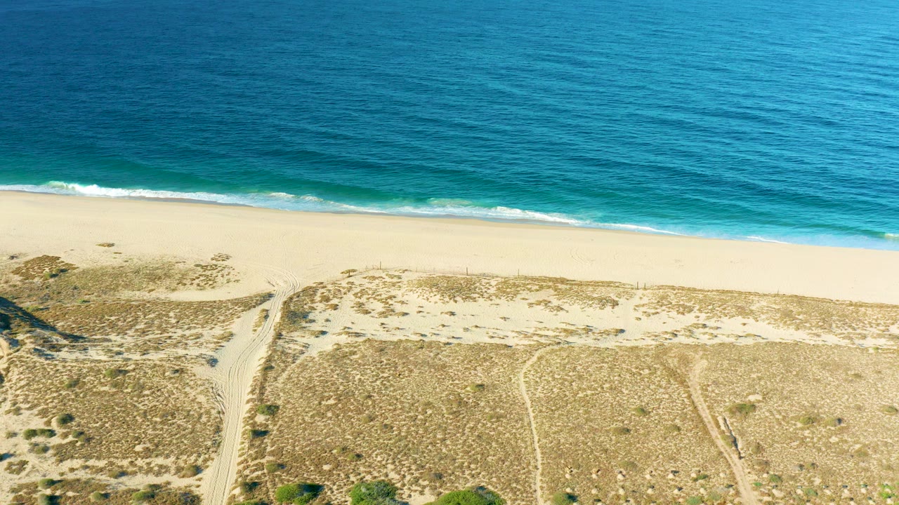 Aerial view of blue ocean, sandy beach, dunes, and sandy paths.