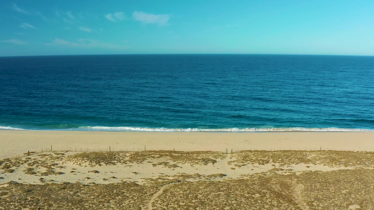 Elevated beach view with dunes, rolling waves, ocean, and sky.
