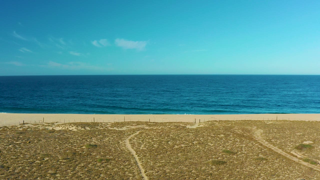 Wide coastal view with ocean, beach, dunes, and sandy paths.