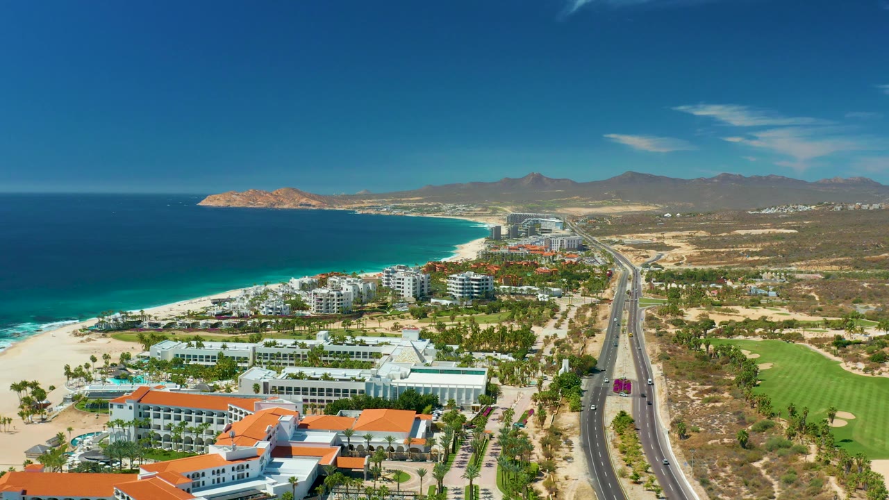 Aerial view of sandy beach, ocean, road, buildings, and green course