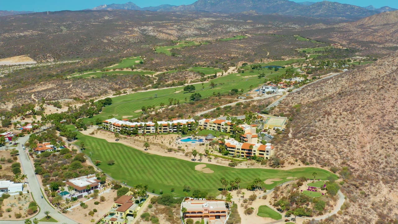 High aerial view of fairways, resort-style buildings, roads, and desert hills.