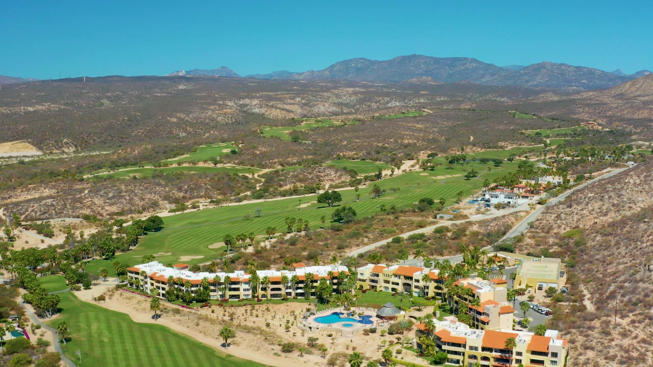 Aerial view of resort buildings, golf fairways, dry hills, and mountains.