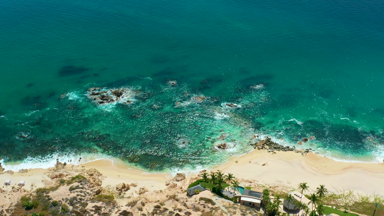 Aerial ocean water breaking over rocks beside a sandy shore