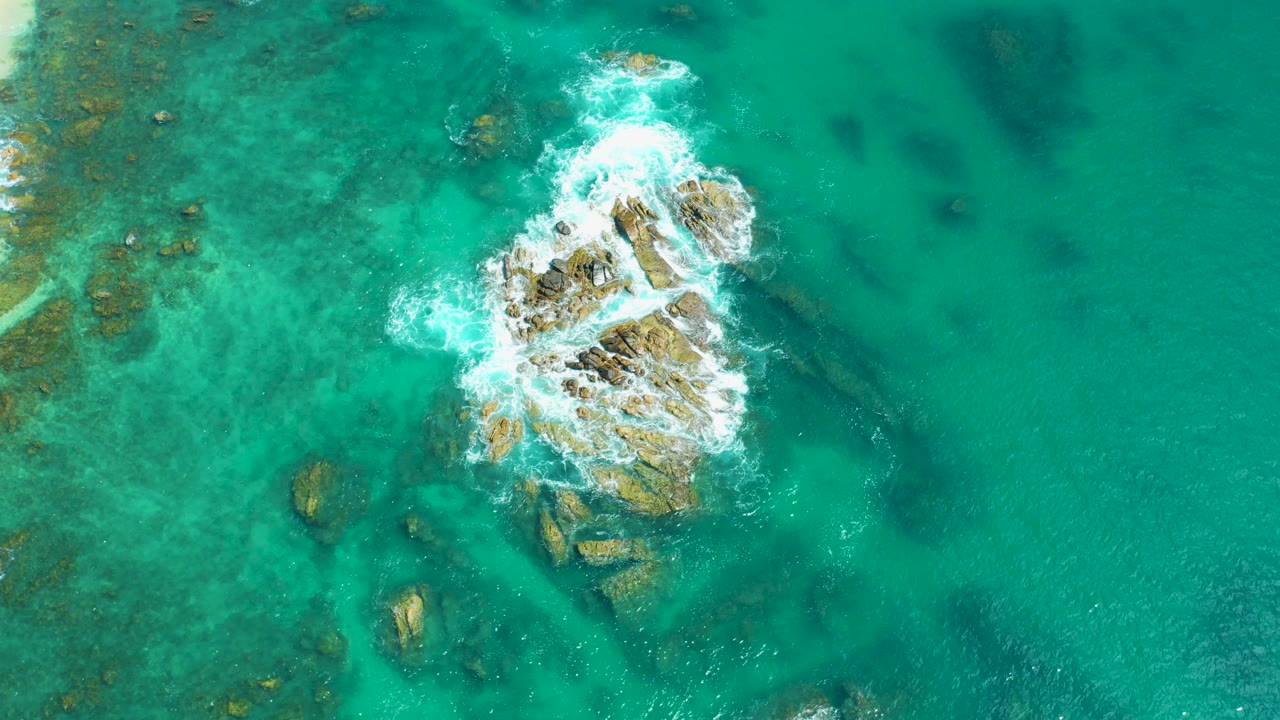 Turquoise ocean water around a rocky outcrop with white surf.
