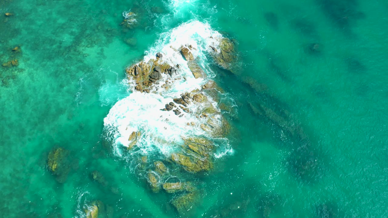 Aerial frame from Marquis Los Cabos, Mexico, with white waves spreading wider over the central rocks in clear turquoise water and no visible people.