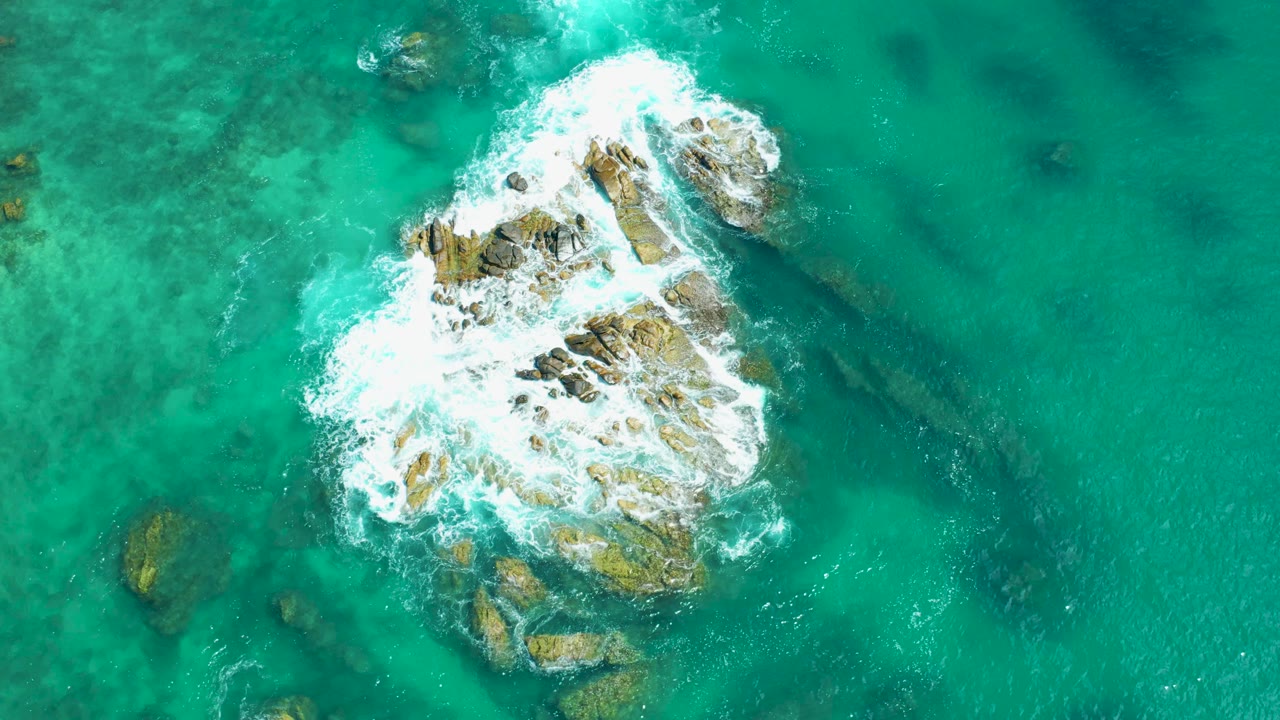 Breaking surf covers the left side of a shallow rock formation.