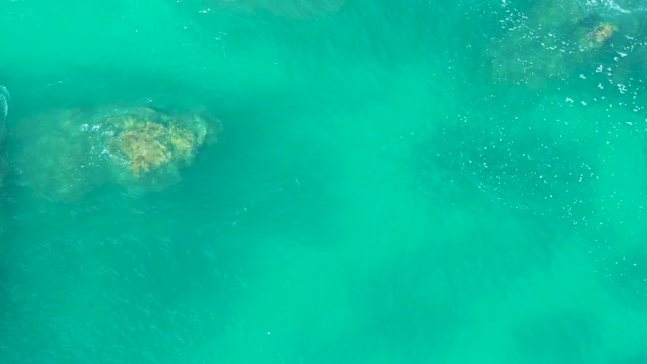 Overhead view of turquoise water at Marquis Los Cabos, Mexico, with a submerged rock near the upper left and no visible people.