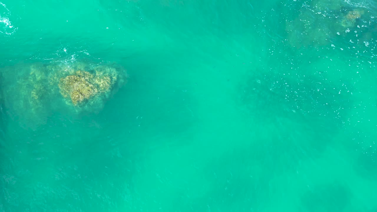 Clear turquoise water at Marquis Los Cabos with the submerged rock closer to the top center and faint ripples crossing the surface, no visible people.