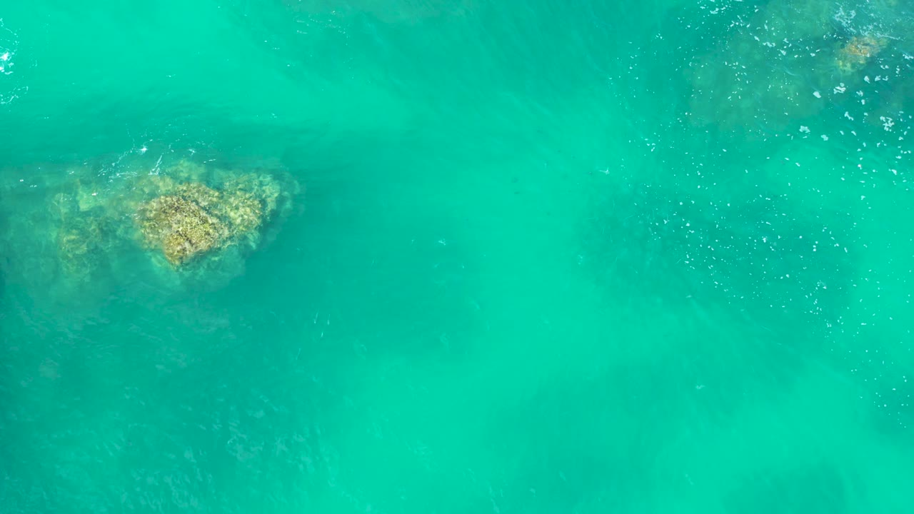 A tan submerged rock is visible along the left side under clear turquoise water at Marquis Los Cabos, with small ripples and no visible people.