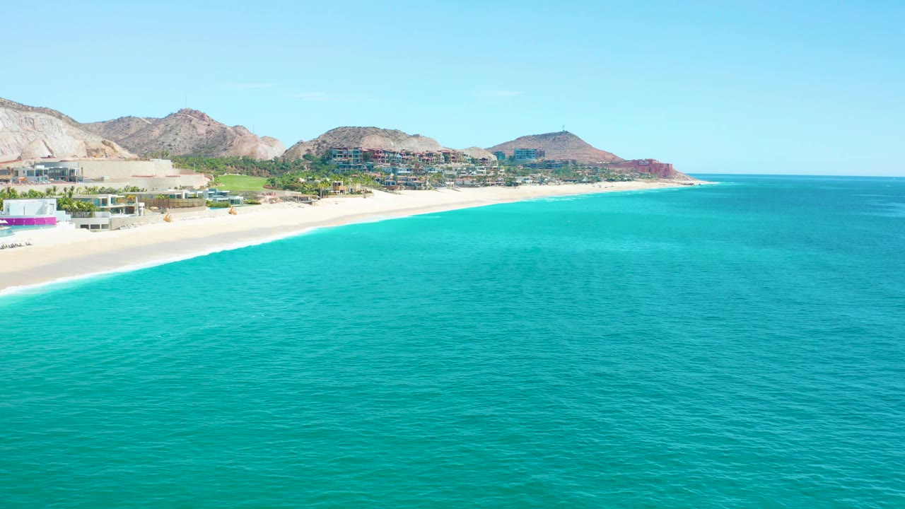 Beach and coastal buildings seen beyond turquoise ocean water.