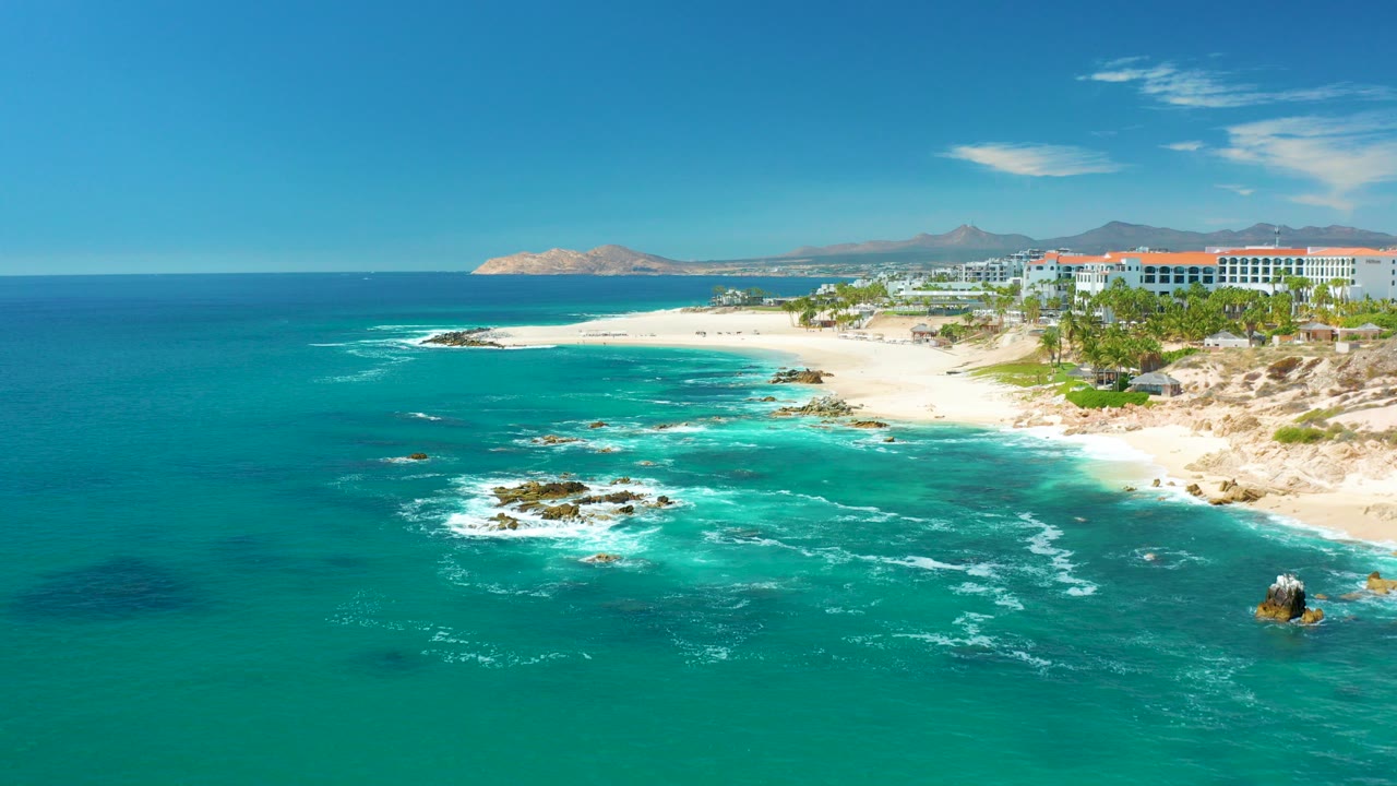 Aerial view of turquoise surf, sandy beach, rocks, and resort buildings.
