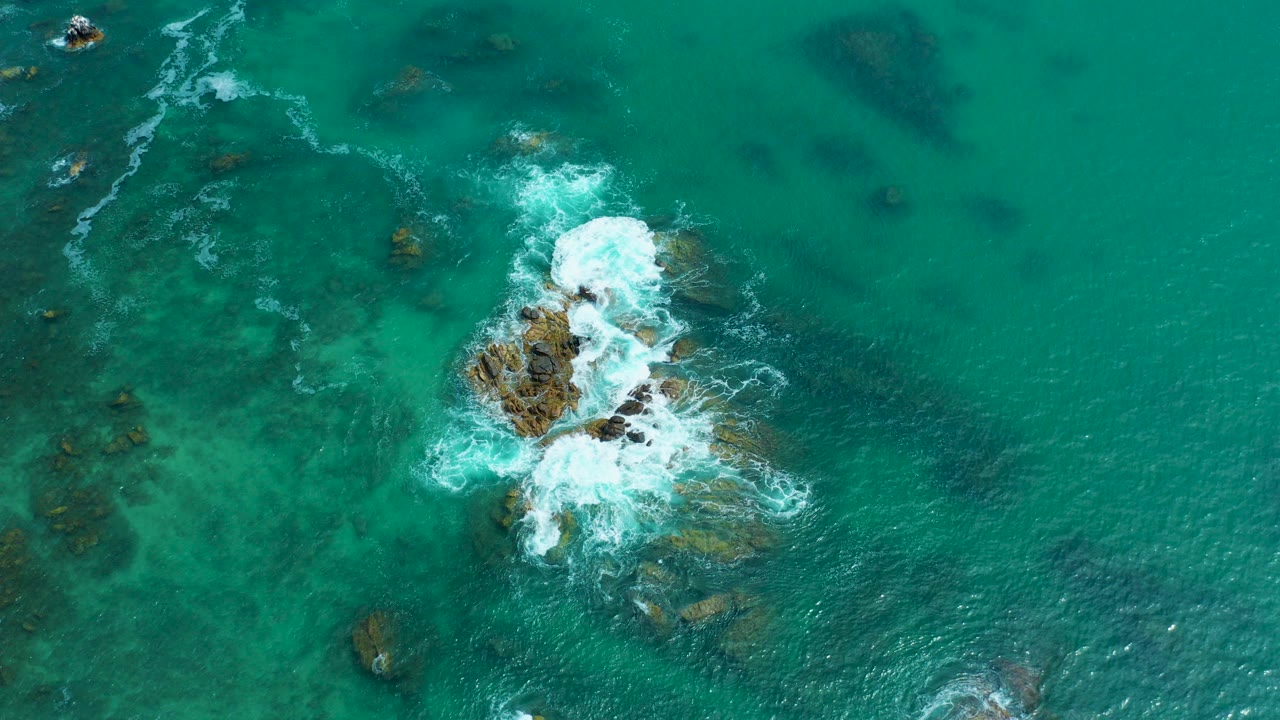 Turquoise ocean water breaking over a small rocky seabed formation.
