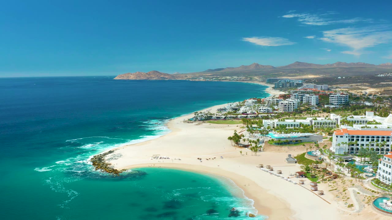 Wide coastal resort beach with blue water and mountains beyond