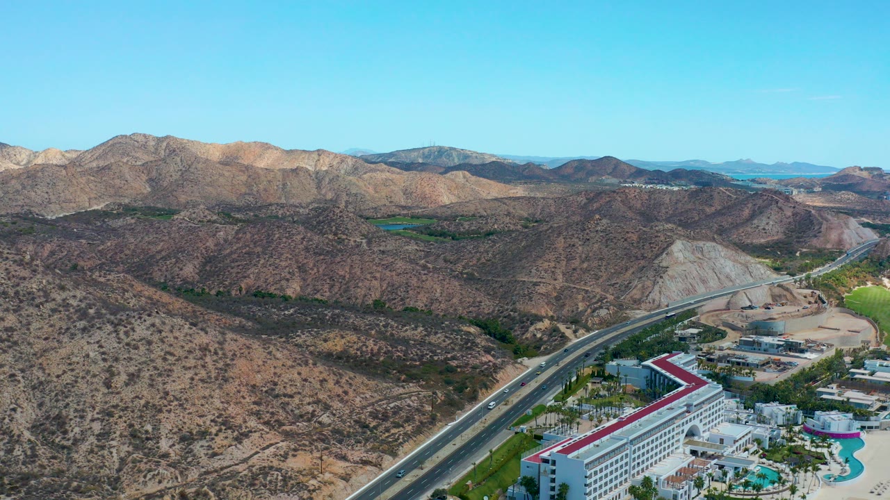 Aerial view of desert highway, red-roof hotel, arid hills, and distant mountains