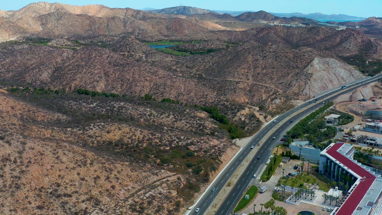 Highway traffic below arid hills with a building complex beside the road.