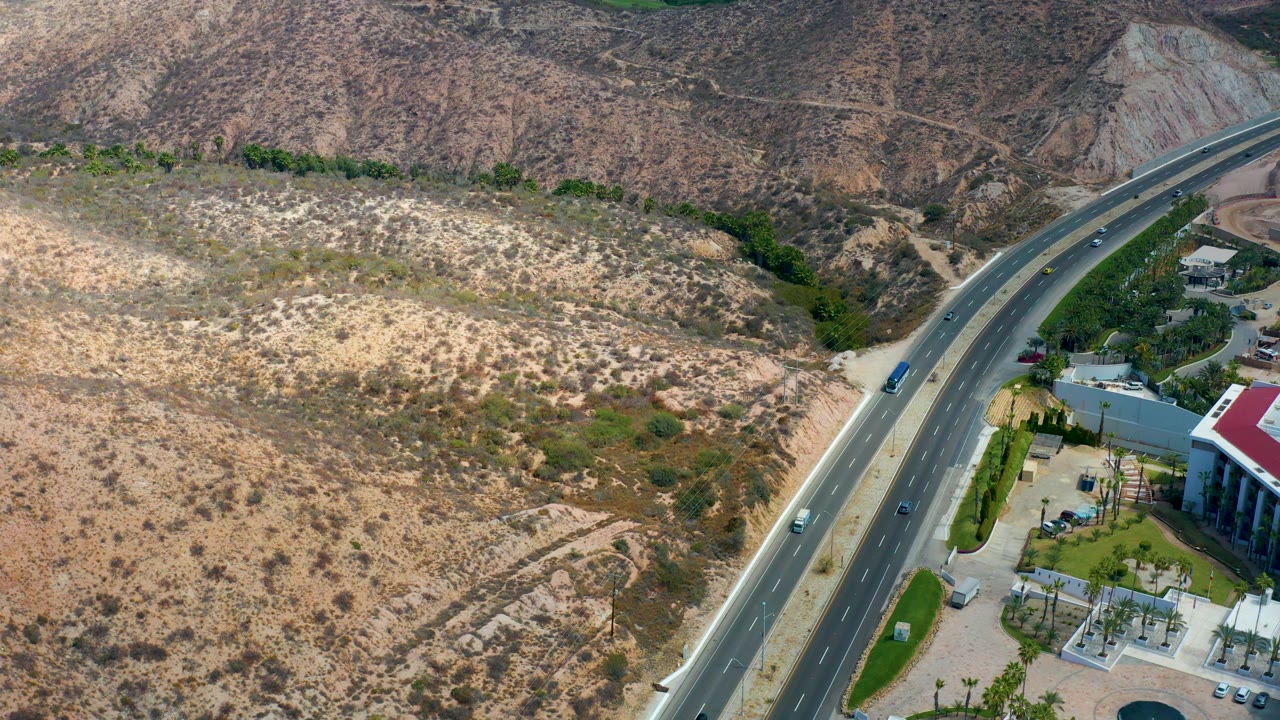 Marquis Los Cabos, Mexico aerial frame with the divided highway cutting diagonally through scrubby tan hills, a few cars and a truck visible, and no visible people.